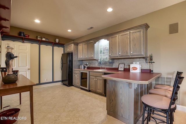 kitchen with visible vents, wine cooler, a peninsula, freestanding refrigerator, and a sink