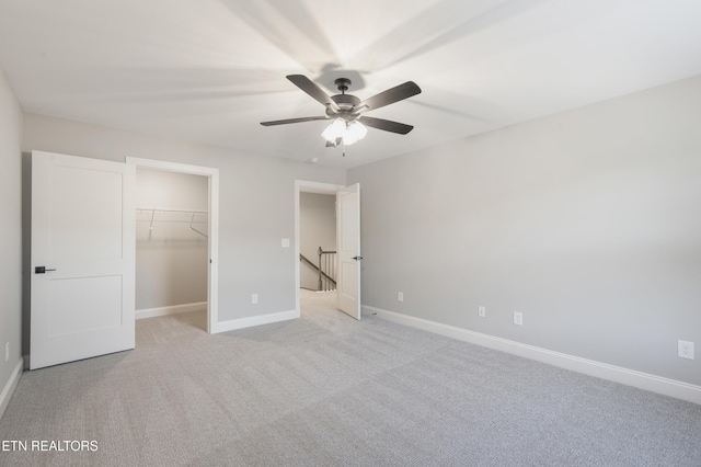 unfurnished bedroom with a closet, a spacious closet, ceiling fan, light colored carpet, and baseboards