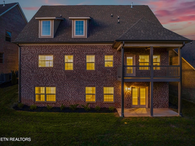 back house at dusk featuring a balcony, a lawn, and a patio