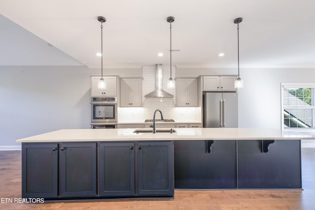 kitchen featuring wall chimney exhaust hood, light hardwood / wood-style floors, hanging light fixtures, a large island, and appliances with stainless steel finishes