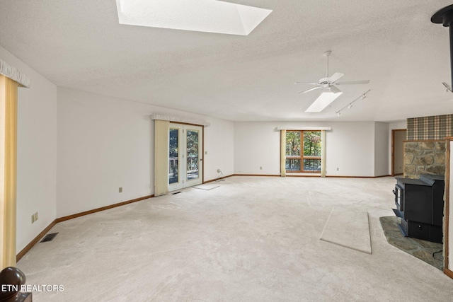 unfurnished living room featuring light carpet, a textured ceiling, a wood stove, and a skylight