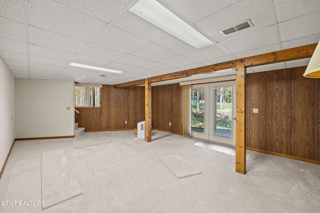 basement featuring a drop ceiling, wooden walls, and light colored carpet