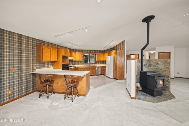 kitchen featuring kitchen peninsula, a wood stove, a breakfast bar, stainless steel dishwasher, and white fridge