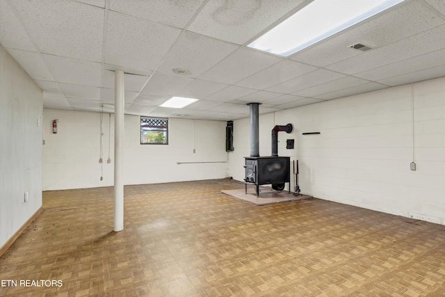 basement featuring a wood stove, a paneled ceiling, and parquet flooring