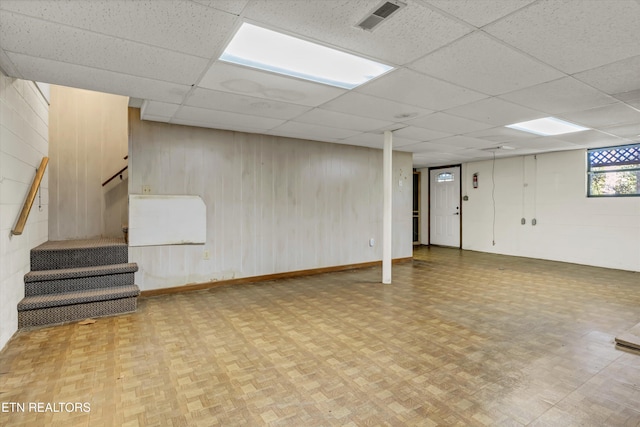 basement featuring parquet flooring, a drop ceiling, and wood walls