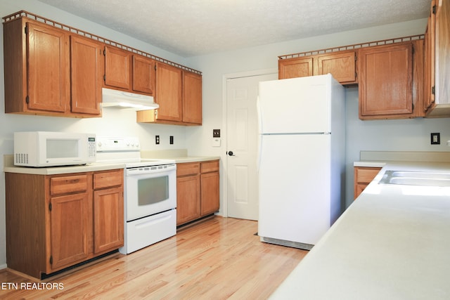 kitchen with white appliances, sink, light hardwood / wood-style floors, and a textured ceiling