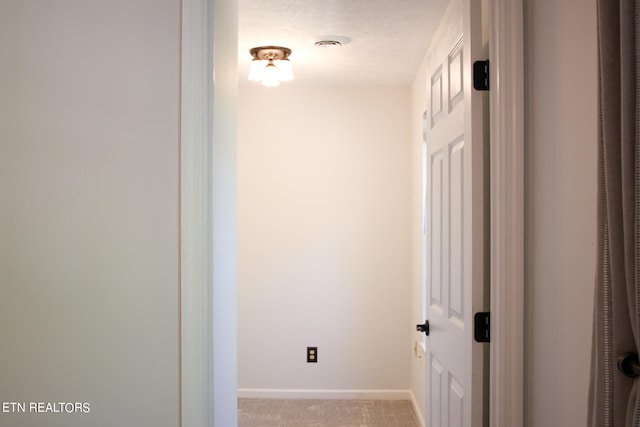 hallway featuring light colored carpet and a textured ceiling