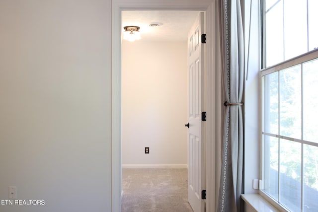 hallway featuring light colored carpet and a textured ceiling