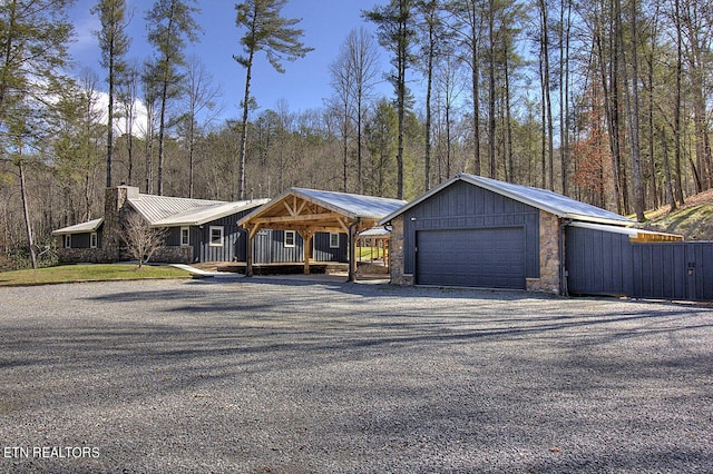 view of front of property featuring stone siding, metal roof, a garage, a chimney, and driveway