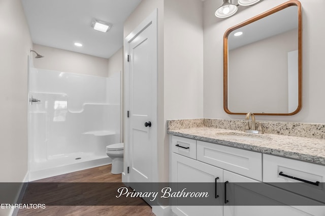 bathroom with hardwood / wood-style floors, toilet, walk in shower, and vanity