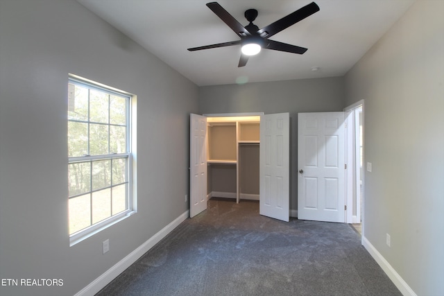 unfurnished bedroom with a closet, a spacious closet, dark carpet, and ceiling fan