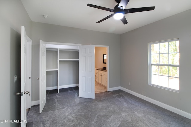 unfurnished bedroom featuring a closet, connected bathroom, dark carpet, and ceiling fan