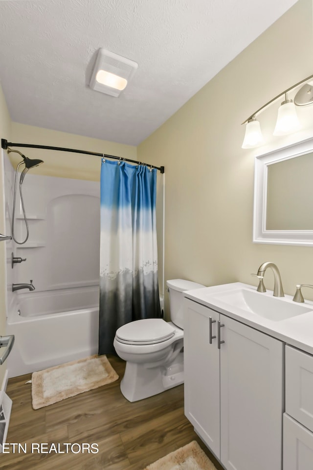 full bathroom with toilet, hardwood / wood-style floors, shower / bath combo with shower curtain, vanity, and a textured ceiling