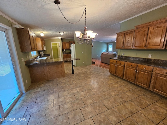 kitchen with sink, an inviting chandelier, a textured ceiling, ornamental molding, and pendant lighting