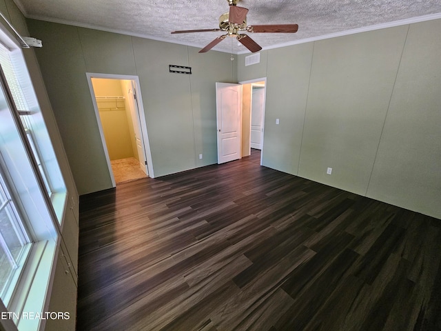 unfurnished bedroom featuring crown molding, a spacious closet, a textured ceiling, dark hardwood / wood-style floors, and ceiling fan