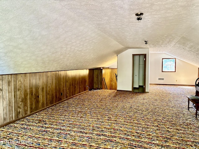 additional living space with wood walls, lofted ceiling, carpet, and a textured ceiling