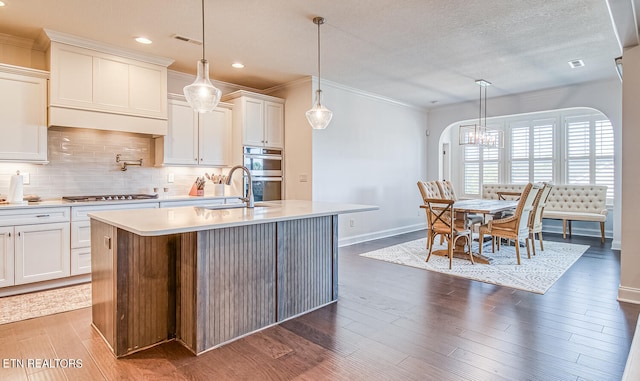 kitchen featuring a kitchen island with sink, dark hardwood / wood-style floors, white cabinets, appliances with stainless steel finishes, and decorative light fixtures