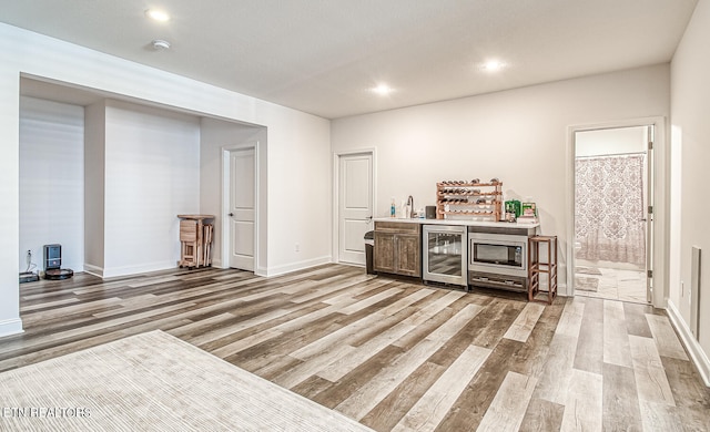 bar featuring beverage cooler, light wood-type flooring, stainless steel microwave, and sink