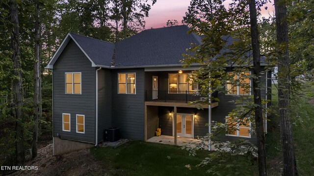 back house at dusk featuring a balcony and central AC