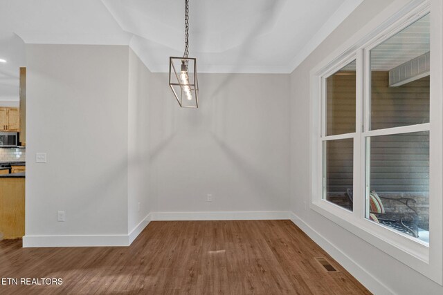 unfurnished dining area featuring crown molding, hardwood / wood-style floors, and a notable chandelier