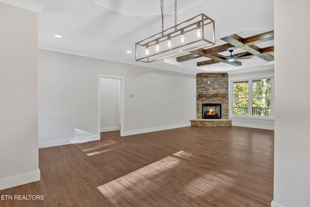 unfurnished living room featuring beam ceiling, coffered ceiling, a stone fireplace, and dark hardwood / wood-style flooring