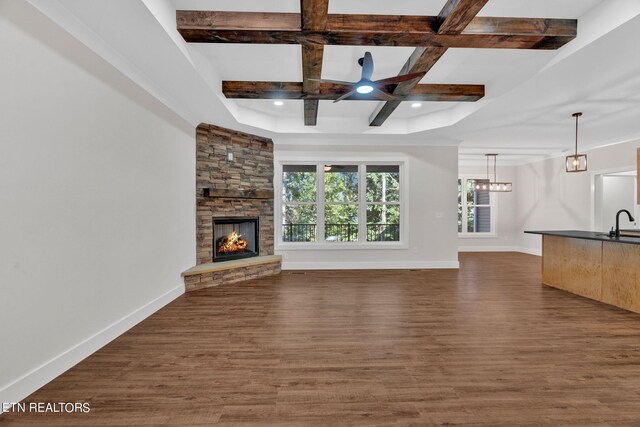 unfurnished living room featuring beam ceiling, coffered ceiling, sink, a stone fireplace, and dark hardwood / wood-style floors