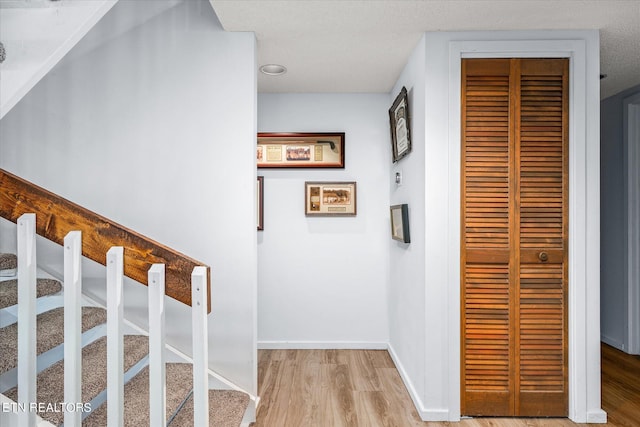 hallway with a textured ceiling and light hardwood / wood-style flooring