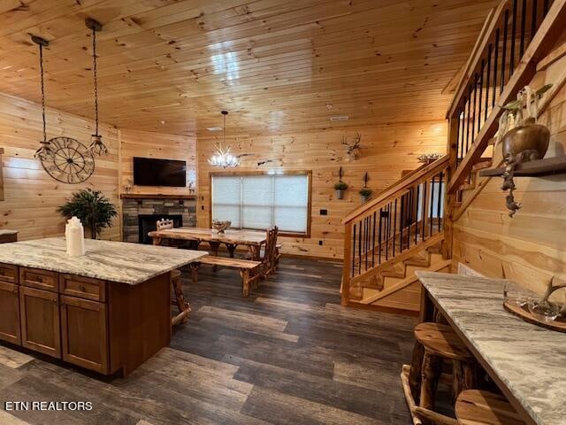 kitchen with light stone counters, wood walls, decorative light fixtures, dark wood-type flooring, and a chandelier