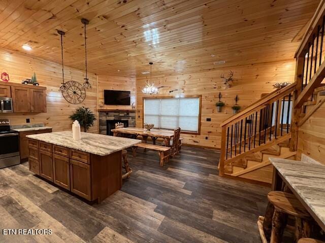 kitchen with a kitchen island, decorative light fixtures, wooden walls, stainless steel appliances, and dark hardwood / wood-style flooring