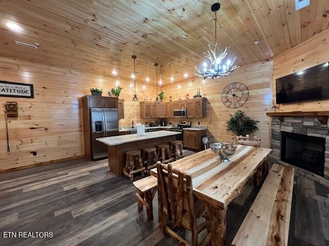 dining space featuring wood walls, a stone fireplace, a chandelier, wooden ceiling, and dark hardwood / wood-style flooring