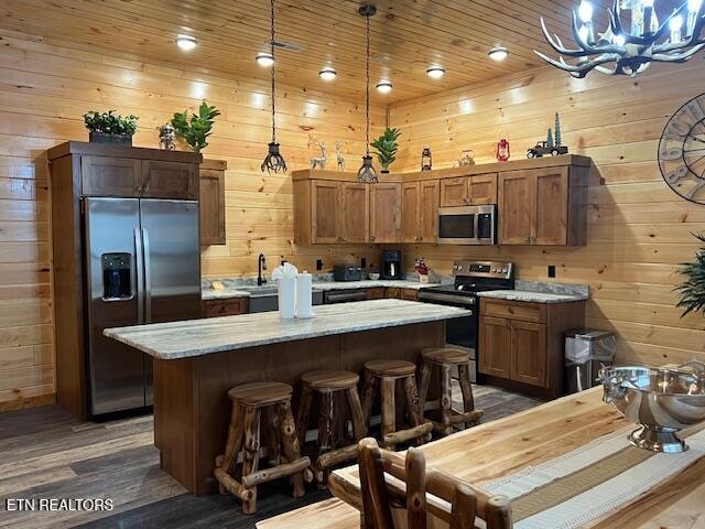 kitchen with wood-type flooring, pendant lighting, wooden walls, and stainless steel appliances