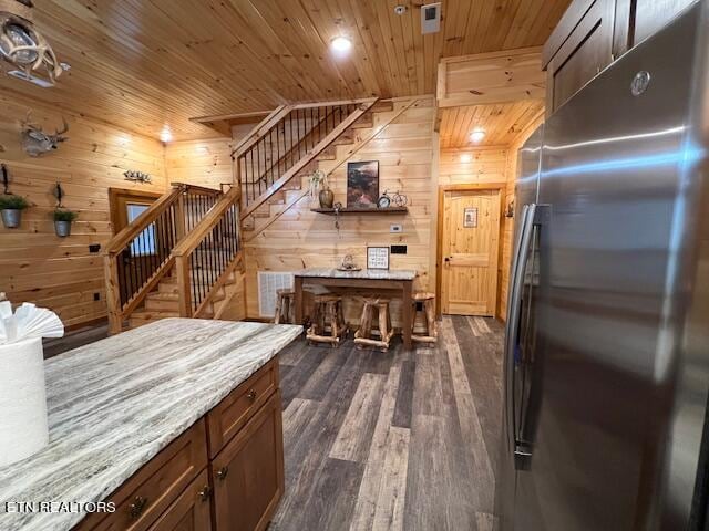 kitchen with wooden walls, dark wood-type flooring, stainless steel refrigerator, wooden ceiling, and light stone countertops