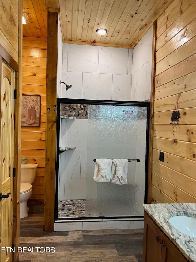 bathroom with wood walls, toilet, hardwood / wood-style floors, a shower with shower door, and vanity