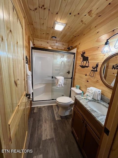 bathroom featuring wooden walls, hardwood / wood-style floors, vanity, a shower with door, and toilet