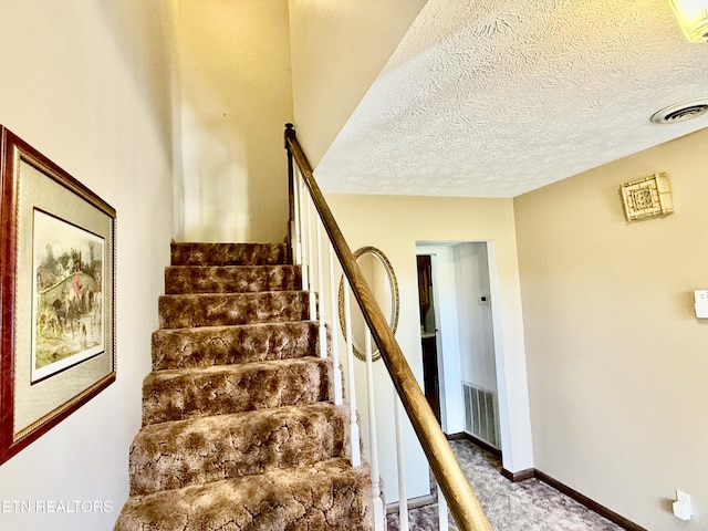 staircase with carpet floors, baseboards, a textured ceiling, and visible vents