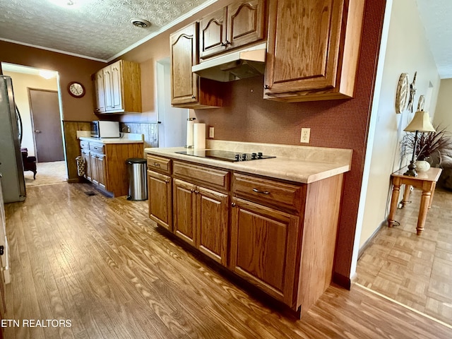 kitchen with wood finished floors, black electric cooktop, light countertops, ornamental molding, and under cabinet range hood