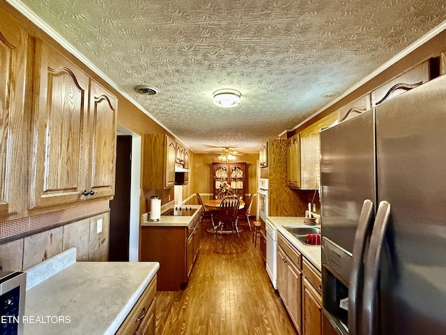 kitchen with stainless steel refrigerator with ice dispenser, crown molding, light countertops, dark wood-style floors, and oven