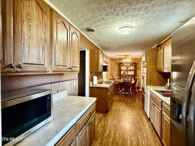 kitchen featuring a ceiling fan, a textured ceiling, appliances with stainless steel finishes, wood finished floors, and light countertops