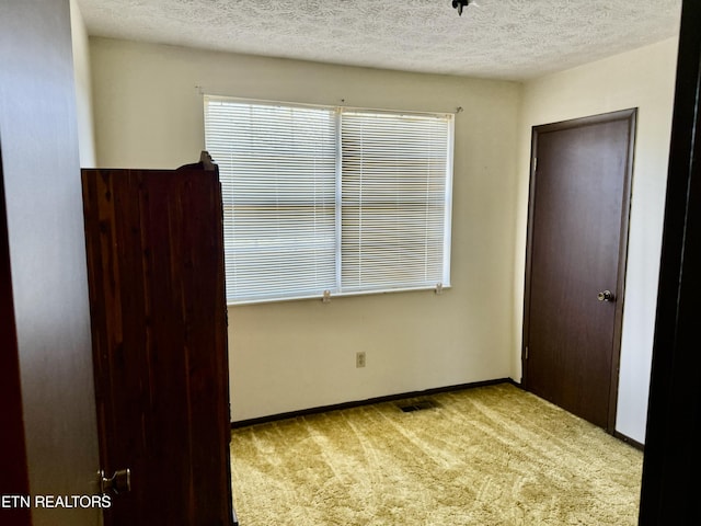 unfurnished bedroom with baseboards, carpet, a textured ceiling, and visible vents