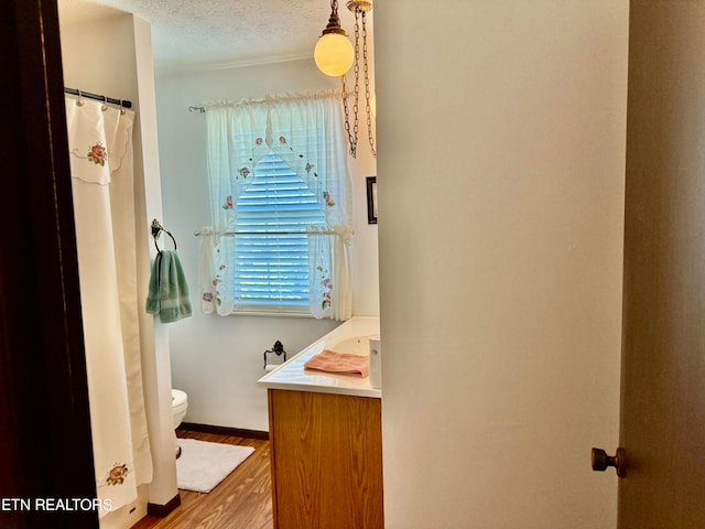 bathroom with a textured ceiling, wood-type flooring, vanity, and toilet