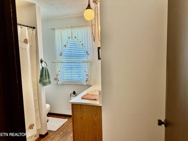 full bathroom featuring vanity, toilet, a textured ceiling, baseboards, and wood finished floors