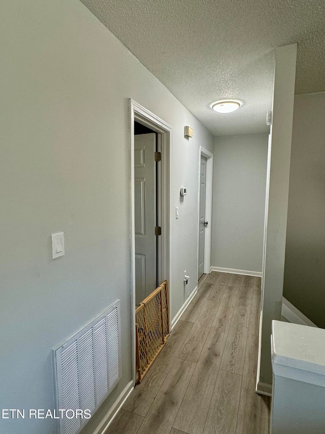 corridor with a textured ceiling, wood finished floors, visible vents, and baseboards