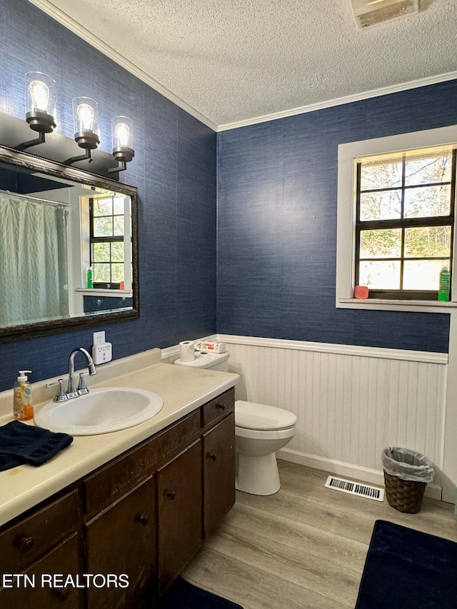 bathroom featuring a textured ceiling, wood finished floors, visible vents, wainscoting, and crown molding