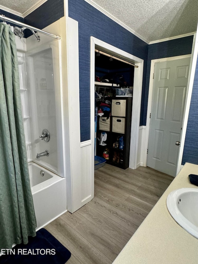 full bath with a textured ceiling, crown molding, a sink, wood finished floors, and shower / bathtub combination with curtain