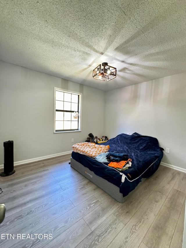 bedroom with a textured ceiling, wood finished floors, and baseboards