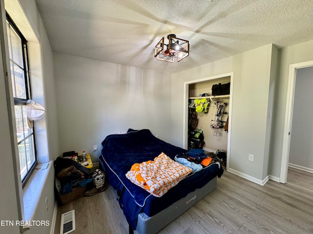 bedroom featuring visible vents, a textured ceiling, baseboards, and wood finished floors