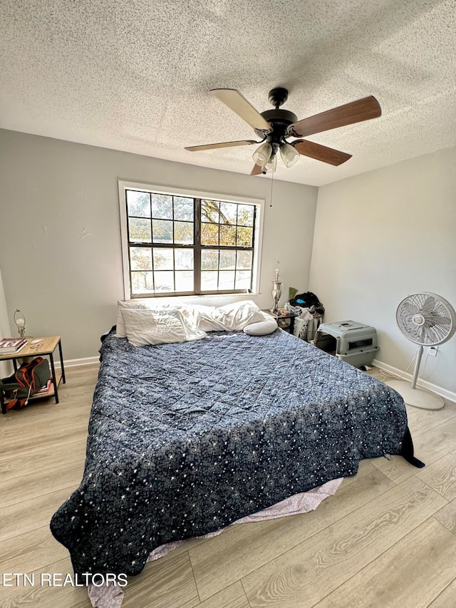 bedroom featuring a ceiling fan, a textured ceiling, baseboards, and wood finished floors