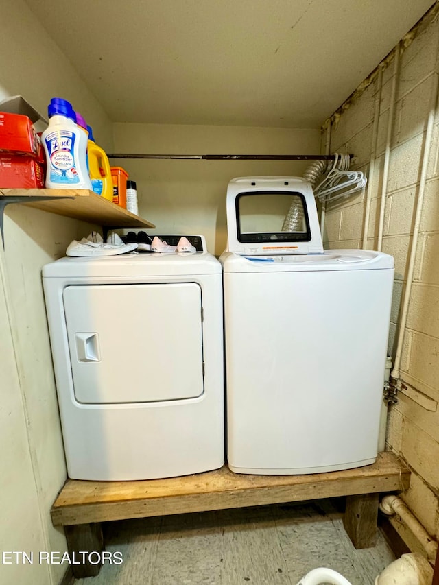 laundry area with concrete block wall and separate washer and dryer