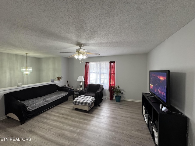 living room featuring ceiling fan with notable chandelier, a textured ceiling, wood finished floors, and baseboards