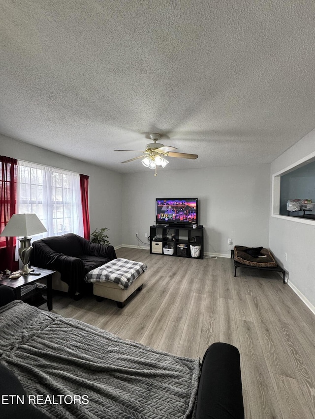 living area with a ceiling fan, a textured ceiling, baseboards, and wood finished floors